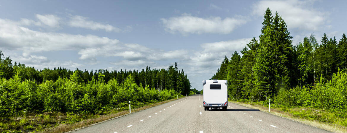 Wohnmobil fährt auf einer Straße zwischen Wäldern in Skandinavien