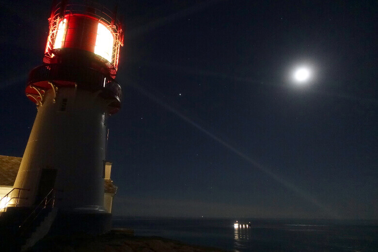 Lindesnes Leuchtturm und vorbeifahrendes Schiff bei Nacht