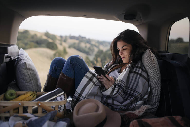 Frau sitzt mit Smartphone in einem Campervan