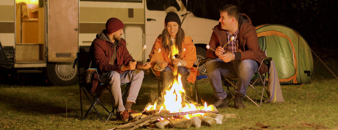 Drei Freunde sitzen vor einem Camper am Lagerfeuer