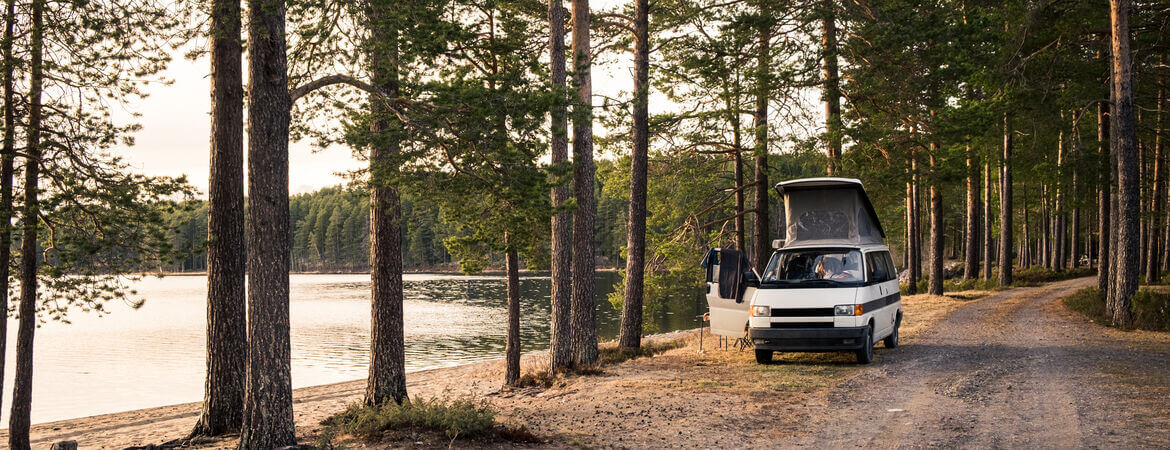 Kleiner Campervan parkt auf einem Waldweg an einem See in Schweden