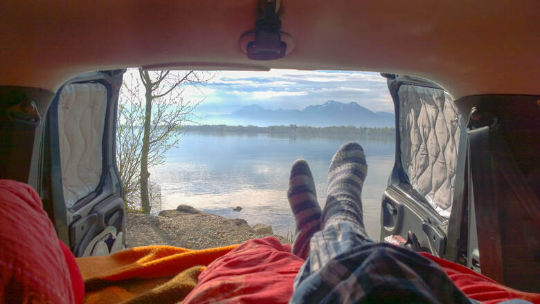 Person liegt im Camper und blickt auf den Chiemsee und die Alpen