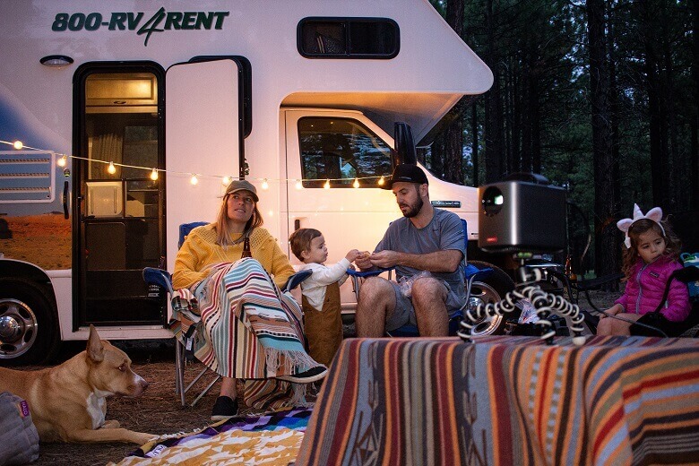 Familie sitzt am Abend auf dem Campingplatz vor dem Wohnmobil