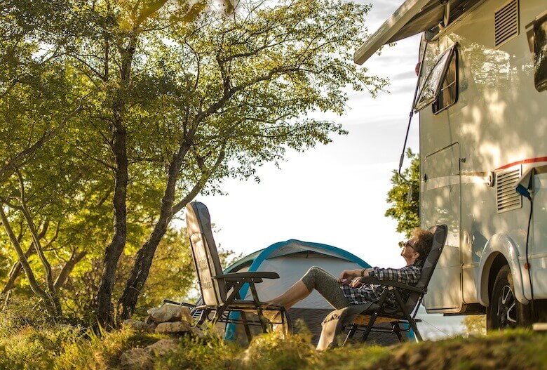 Camping für Senioren: Ältere Dame entspannt sich auf Campingstühlen vor ihrem Wohnmobil.