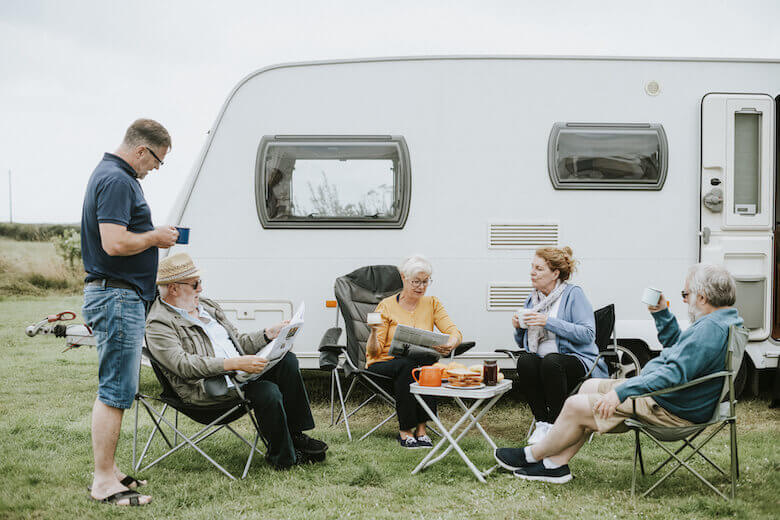 Camping für Senioren: Camper-Pärchen entspannen gemeinsam vor dem Wohnwagen. 