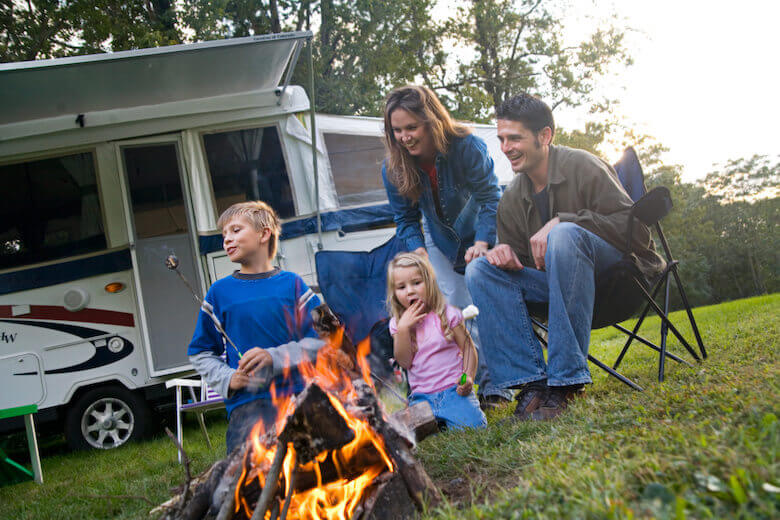 Camping mit Kindern: Familie grillt gemeinsam vor dem Wohnmobil.