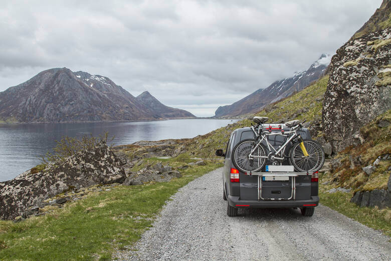 Camper fährt auf Schotterstraße am Fjord