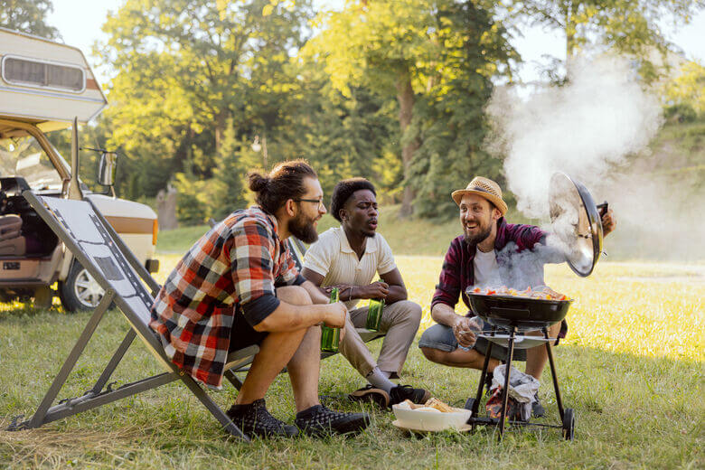 Drei Freunde grillen im Sommer vor einem Wohnmobil