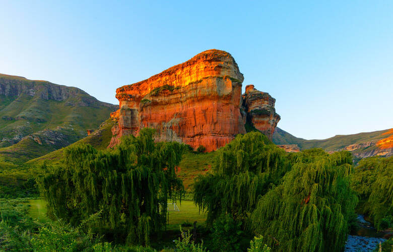 Eine rote Felsformation im Drakensberge Gebirge, angestrahlt von der untergehenden Sonne, mit tiefgrüner Vegetation