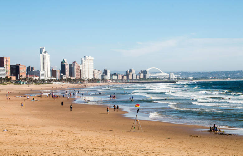 Großer Strandabschnitt vor der Stadt Durban mit Hochhäusern und einem Stadion im Hintergrund