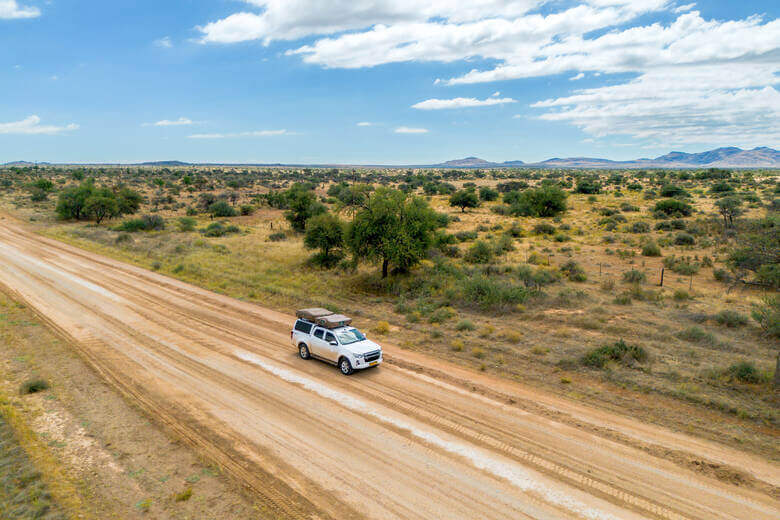 Camper mit Dachzelt fährt durch die Wüste in Namibia