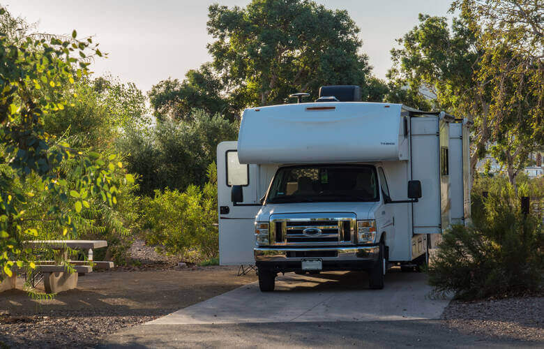 Ein Wohnmobil mit Slideouts steht auf einem Campingplatz umgeben von Bäumen und Büschen