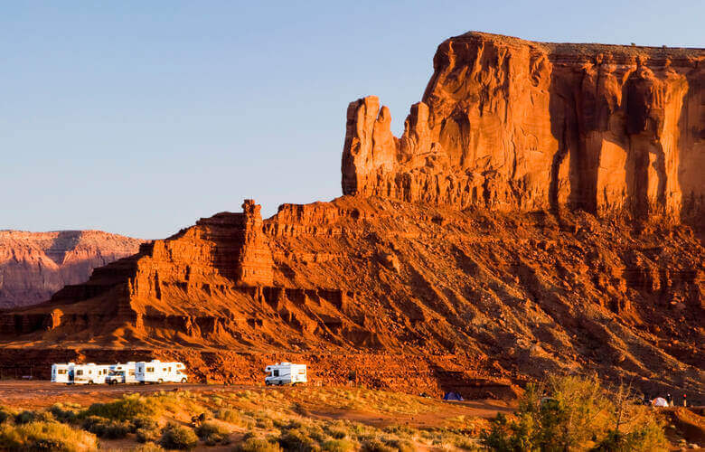 Wohnmobile stehen auf einem Stellplatz in Monument Valley vor einem großen Felsen im Sonnenuntergang