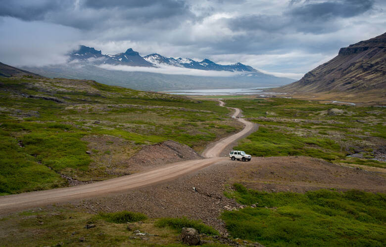 Offroad-Auto entlang einer Schotterstraße in Island mit Bergen im Hintergrund