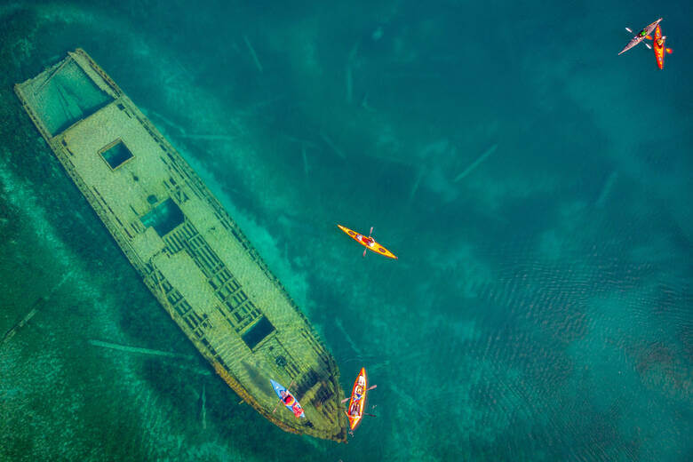 Luftaufnahme eines Schiffswracks von oben mit mehreren Kajaks