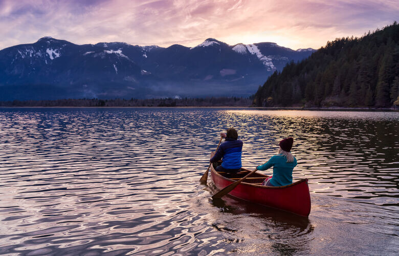 Zwei Menschen fahren bei Sonnenuntergang mit einem Kanu auf dem Harrison River in BC