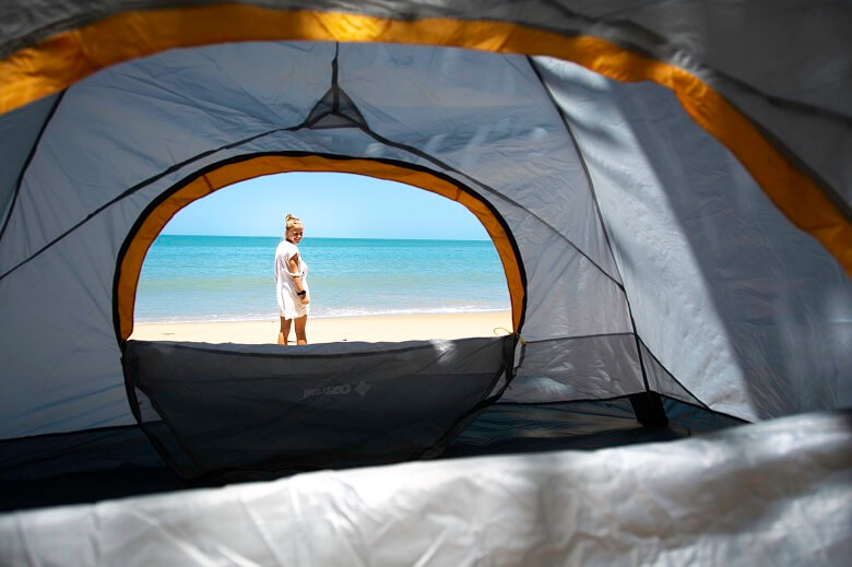 Frau steht an einem Strand in Australien vor einem Zelt 