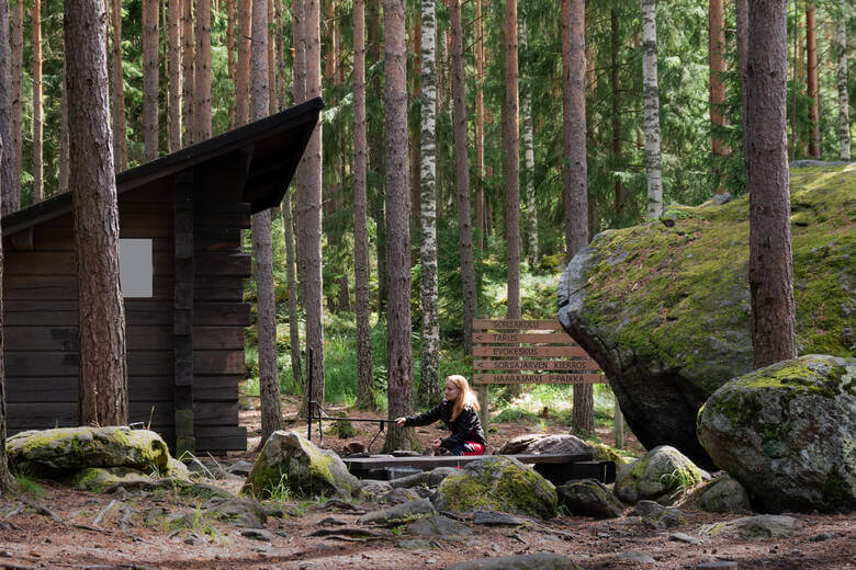 Frau sitzt an einem Lagerfeuer auf einem Campingplatz in Finnland
