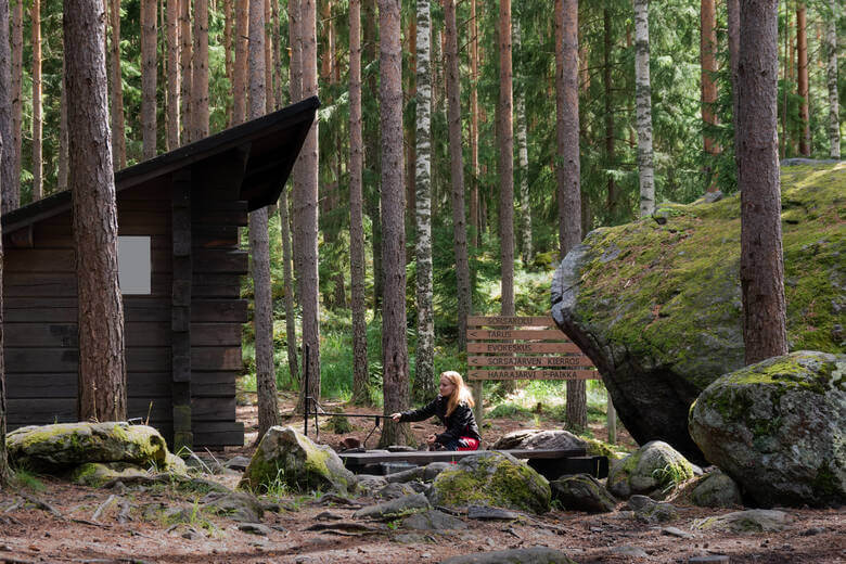 Frau sitzt an einem Lagerfeuer auf einem Campingplatz in Finnland 