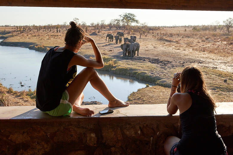 Zwei Frauen beobachten Elefanten an einem Wasserloch in Simbabwe